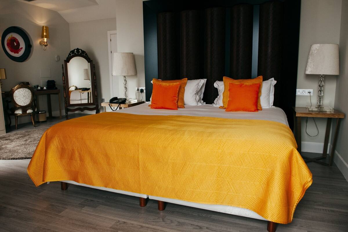A hotel room with a large bed, a nightstand, a desk, a chair, a mirror, and a wall-mounted lamp.
