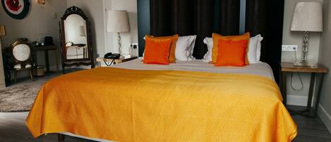 A hotel room with a large bed, a nightstand, a desk, a chair, a mirror, and a wall-mounted lamp.