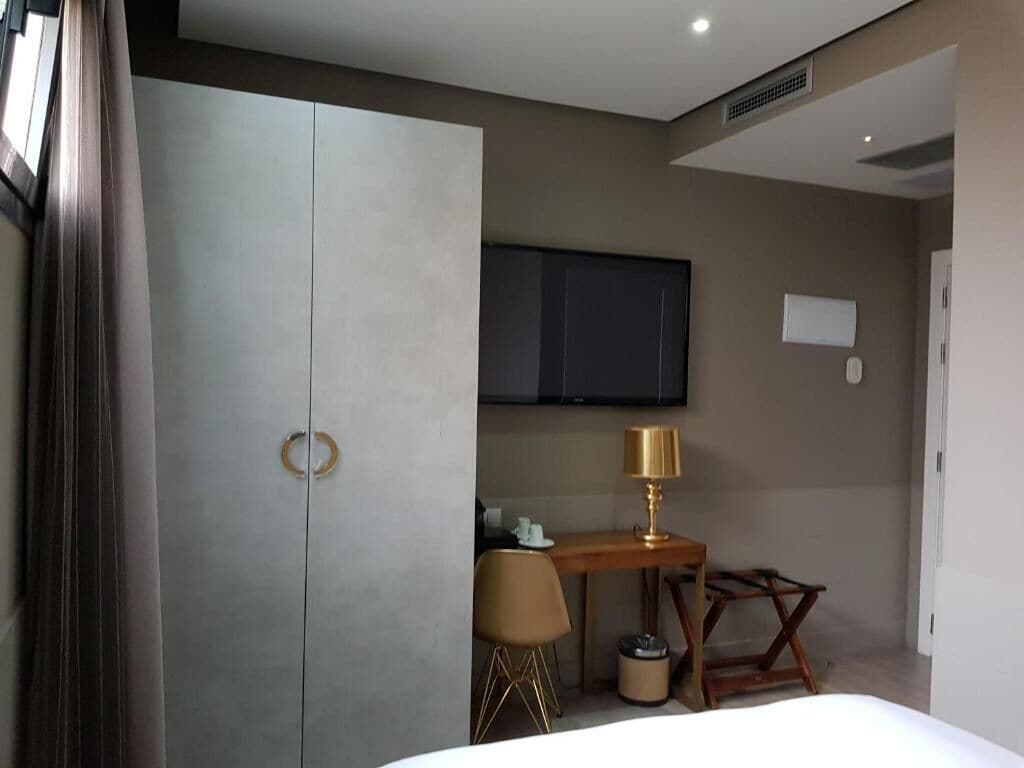 Una habitación de hotel con cama, escritorio, silla, televisor y armario.