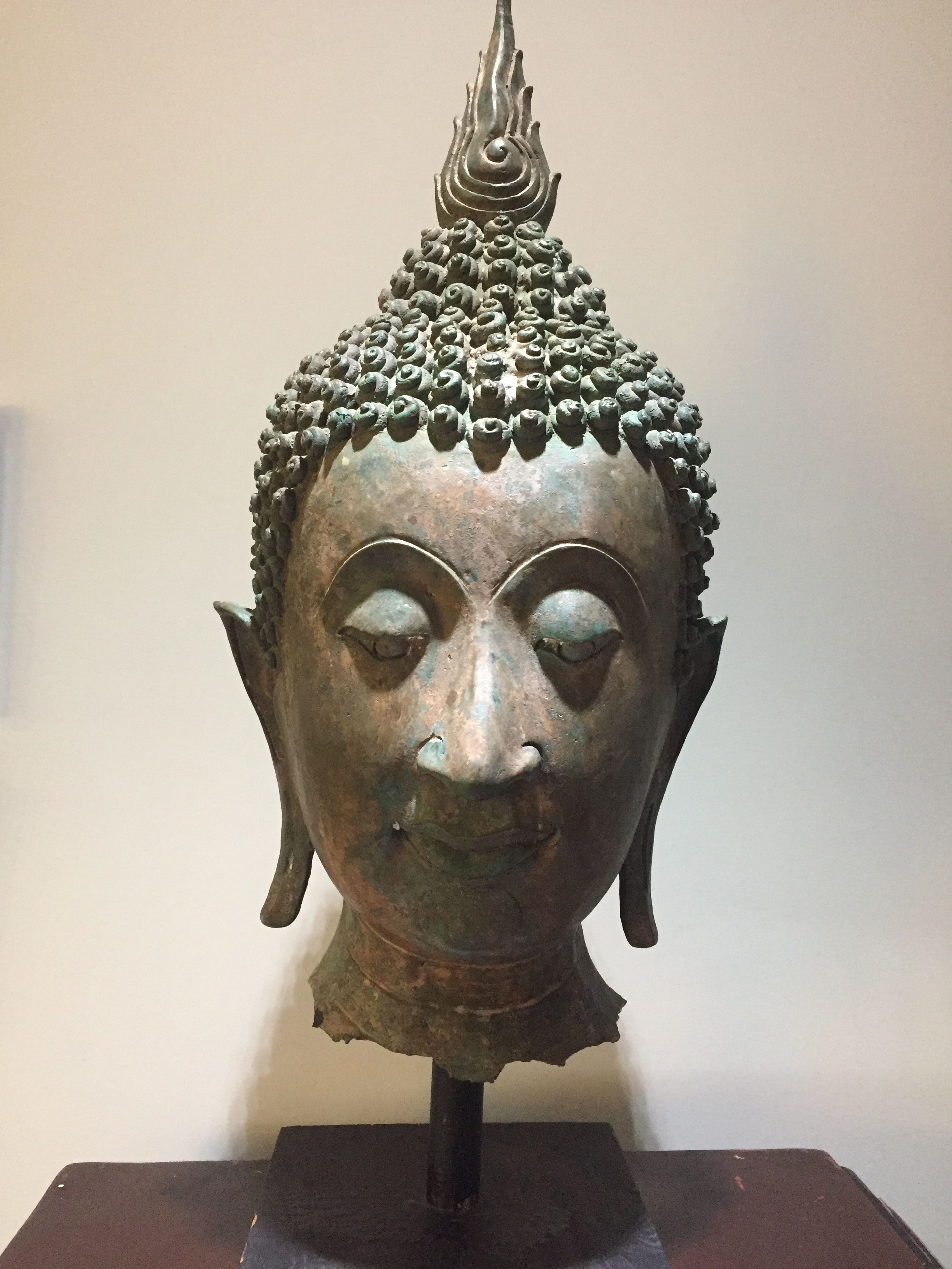 A bronze Buddha head sculpture with a flame-like top, mounted on a dark base.