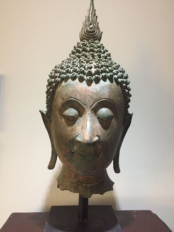 Una escultura de bronce de una cabeza de Buda con un remate en forma de llama, sobre un pedestal oscuro.