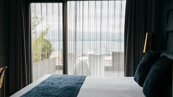 Een hotelkamer met een bed, uitzicht op de stad door dunne gordijnen, en een lamp op het nachtkastje.