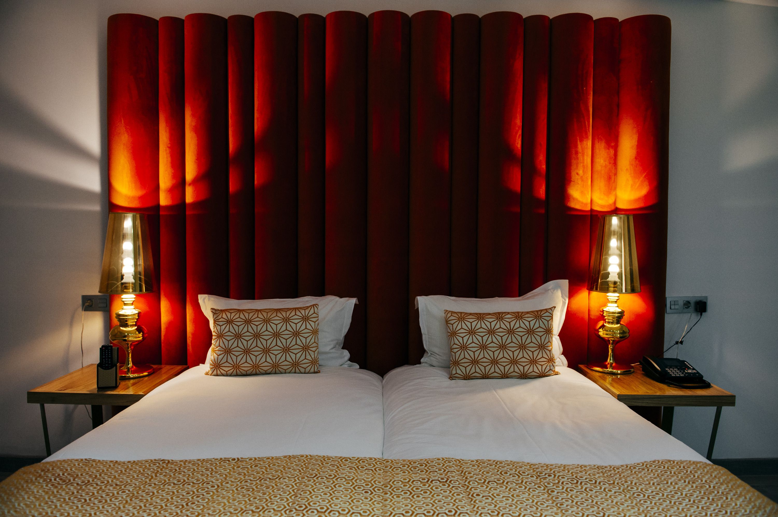 A hotel room with two beds, red curtains, patterned pillows, and bedside lamps.