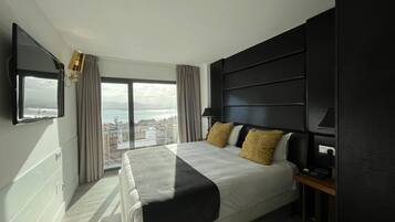 Une chambre d’hôtel moderne dotée d’un grand lit, d’un téléviseur à écran plat fixé au mur et offrant une vue sur la ville par la fenêtre.