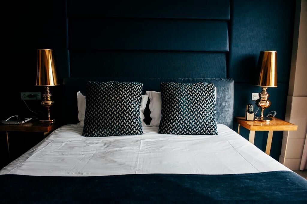 A neatly made bed with white linens, two patterned pillows, and two bedside lamps on wooden nightstands.