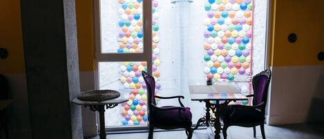 A room with two tables and chairs, a window with colorful circular decorations, and a light fixture.