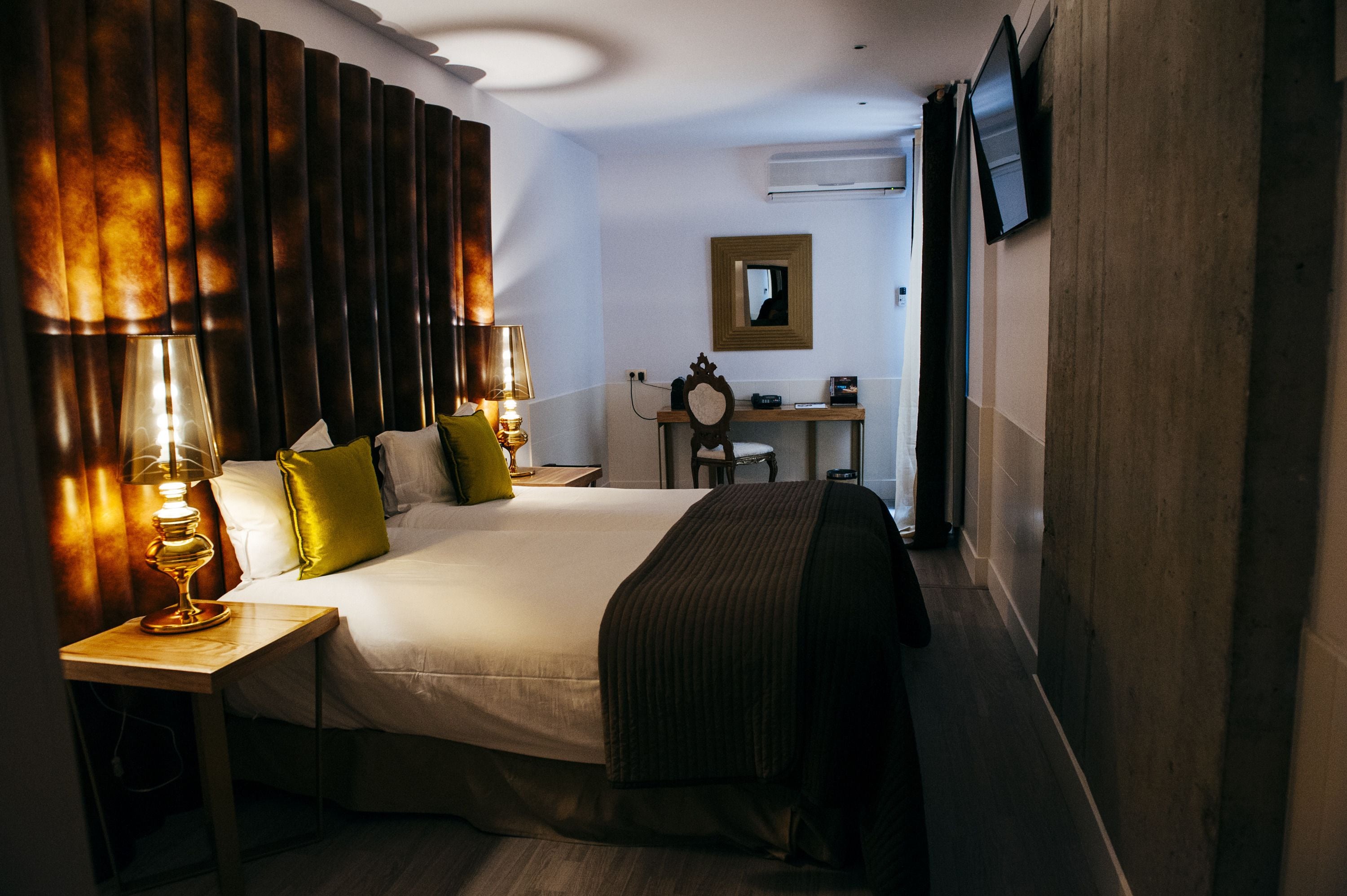 Habitación de hotel con una cama grande, lámparas de noche, un escritorio con espejo y un televisor fijado a la pared.