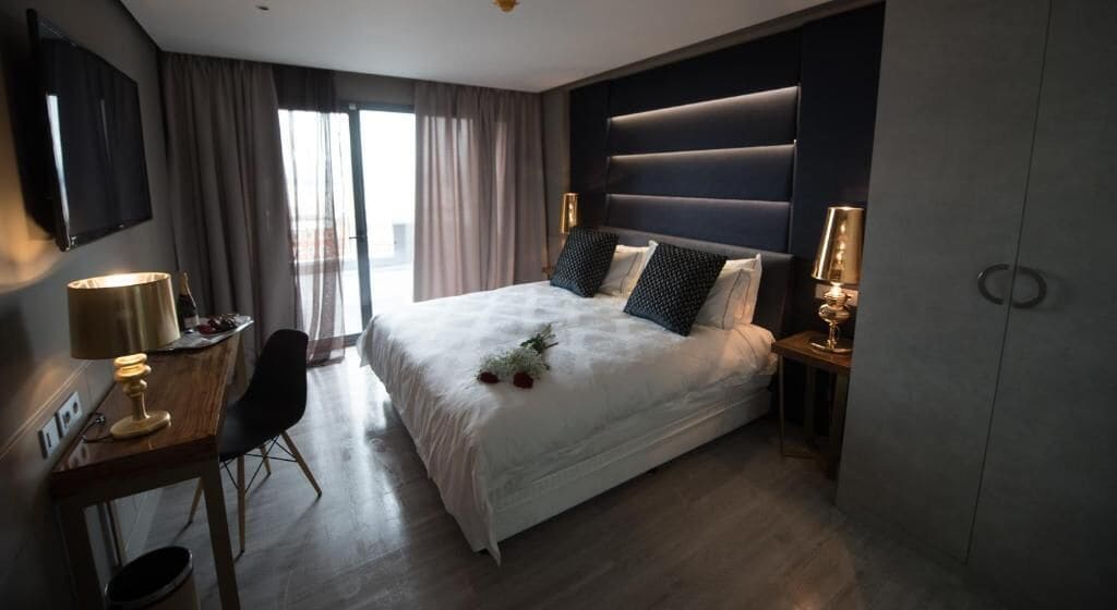 Una camera d'albergo con un letto grande, comodini con lampade, una scrivania e una sedia.