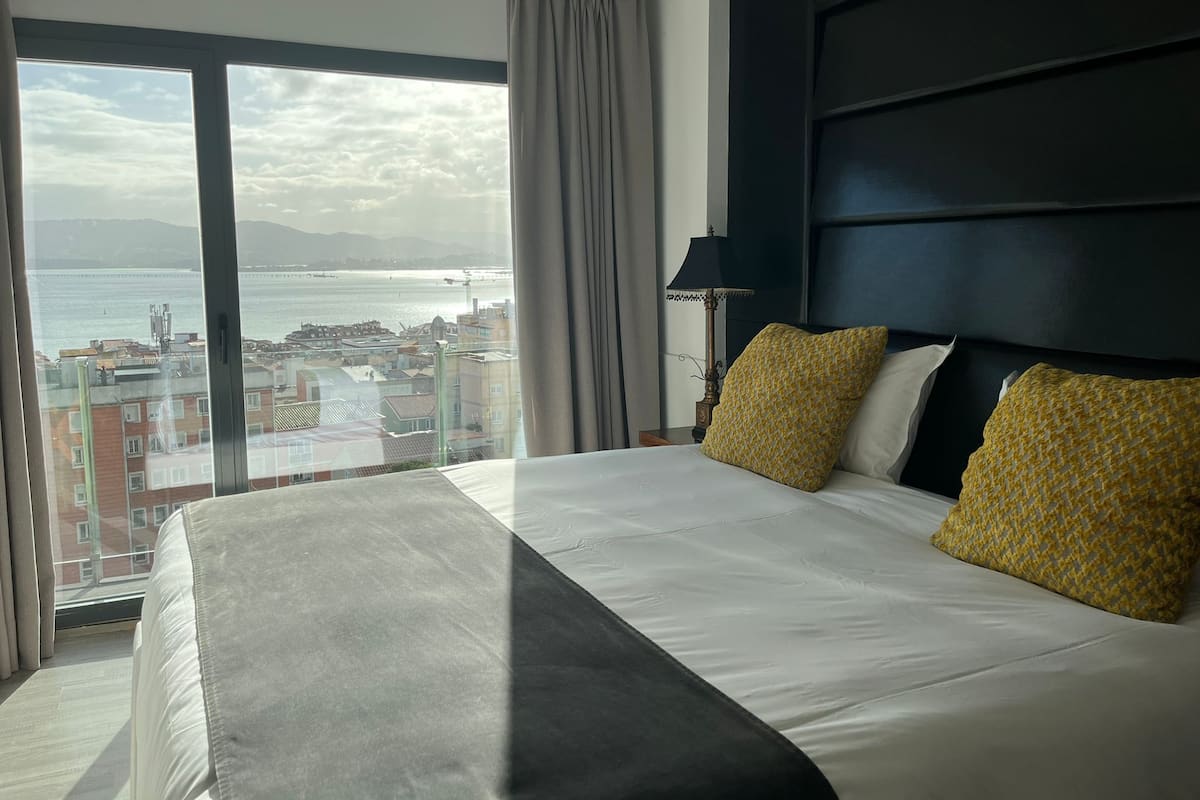 A hotel room with a large bed, a view of the sea, and a cityscape.