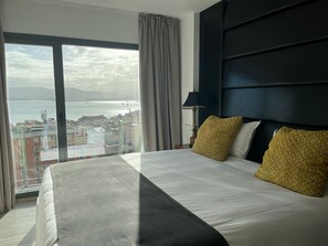 Habitación de hotel con una cama grande, vistas al mar y al paisaje urbano.
