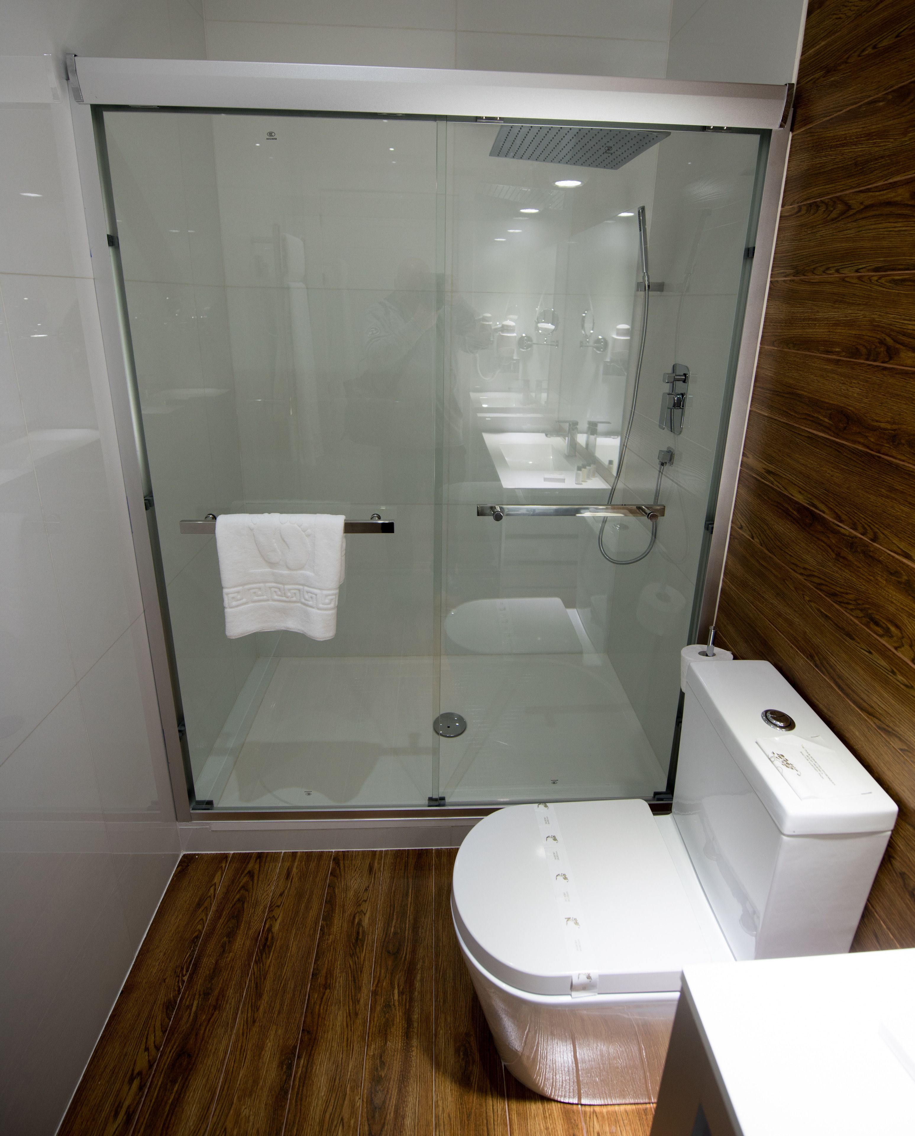 Un baño moderno con ducha de vidrio, inodoro blanco y piso de madera.