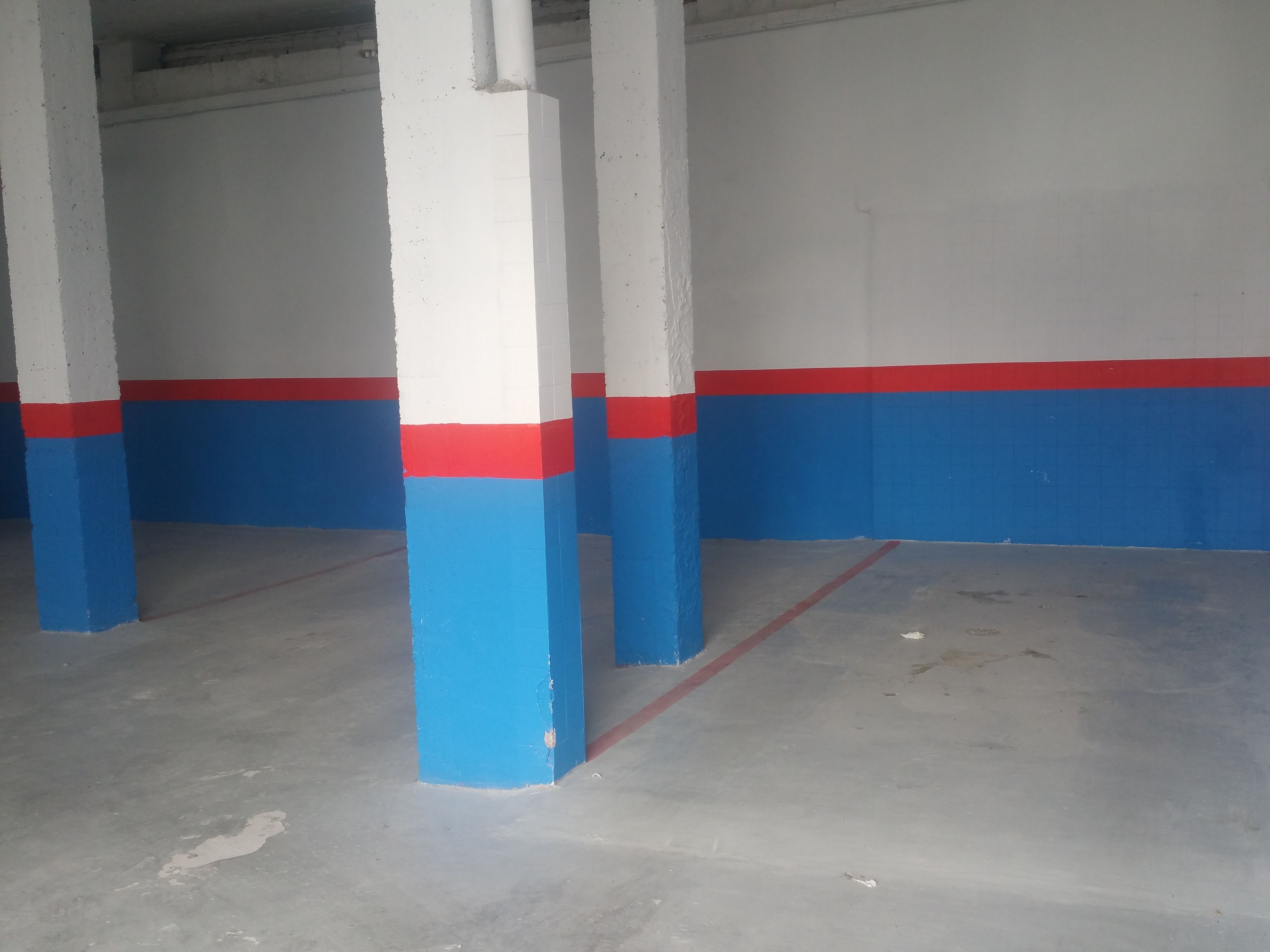 Un garaje para estacionar con columnas pintadas en azul y rojo, y un piso de concreto.