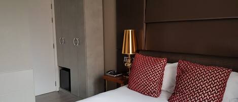 Habitación de hotel con una cama grande, un armario, una mesita de noche con lámpara y almohadones estampados.