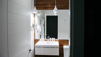 Un baño moderno con lavamanos blanco, paneles de madera e iluminación colgante.
