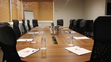 A conference room with a long wooden table, black chairs, and a whiteboard.