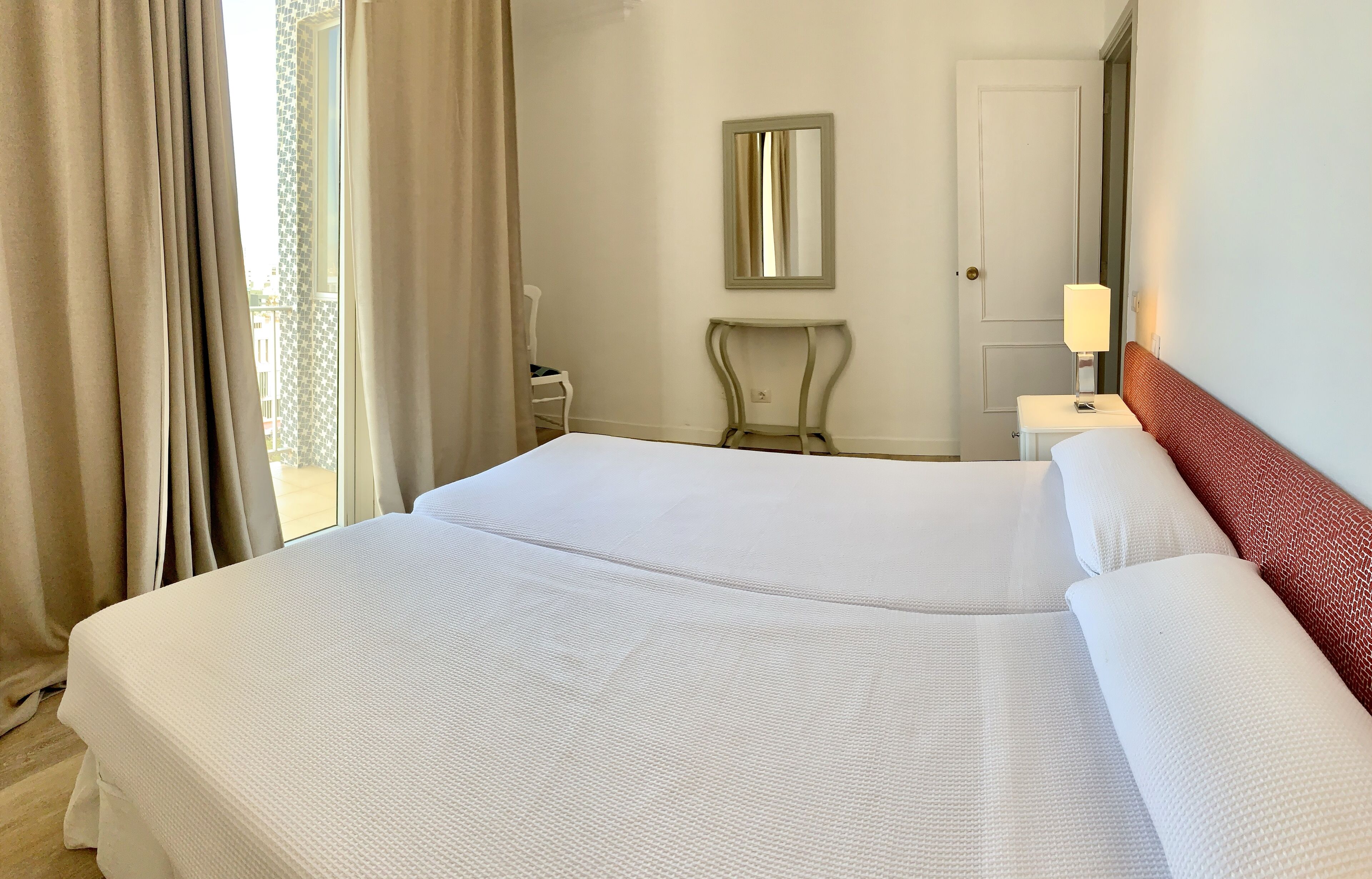 A hotel room with a large bed, a bedside table with a lamp, a chair, and a mirror on the wall.