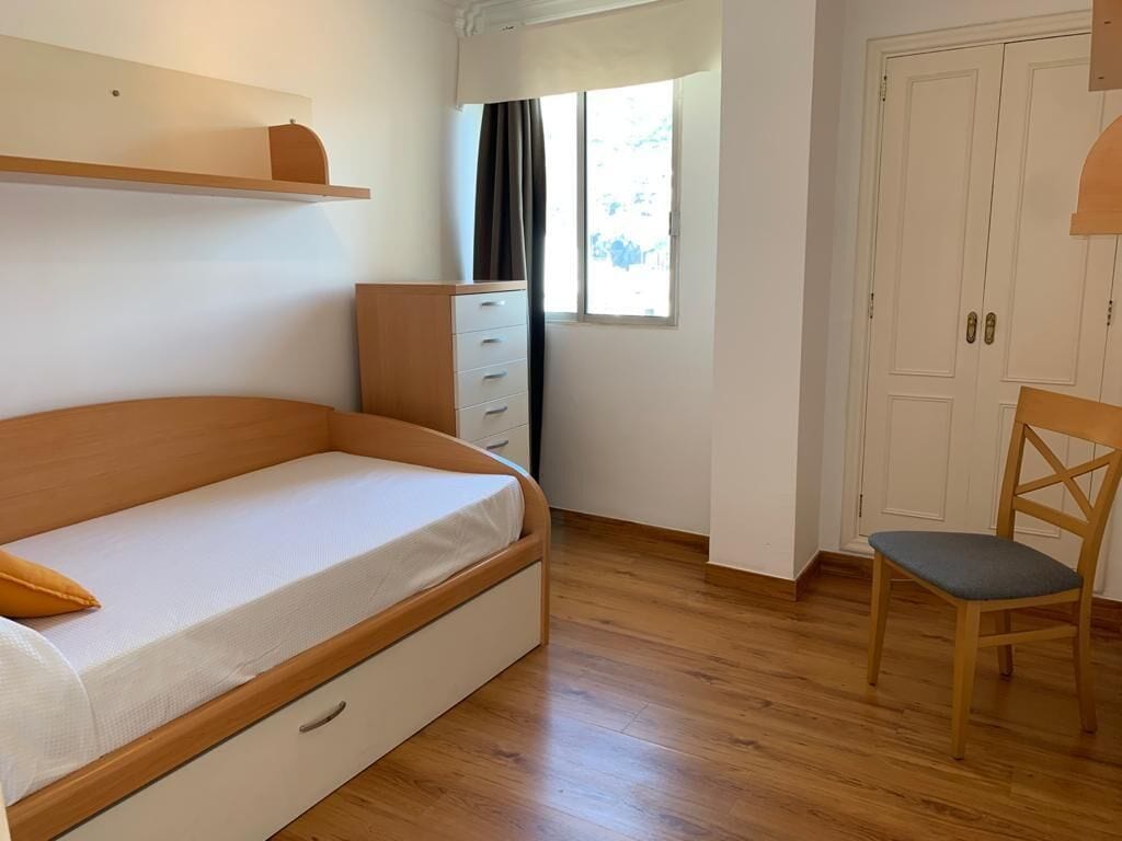 A room with a single bed, a wooden dresser, a chair, and a window with curtains.