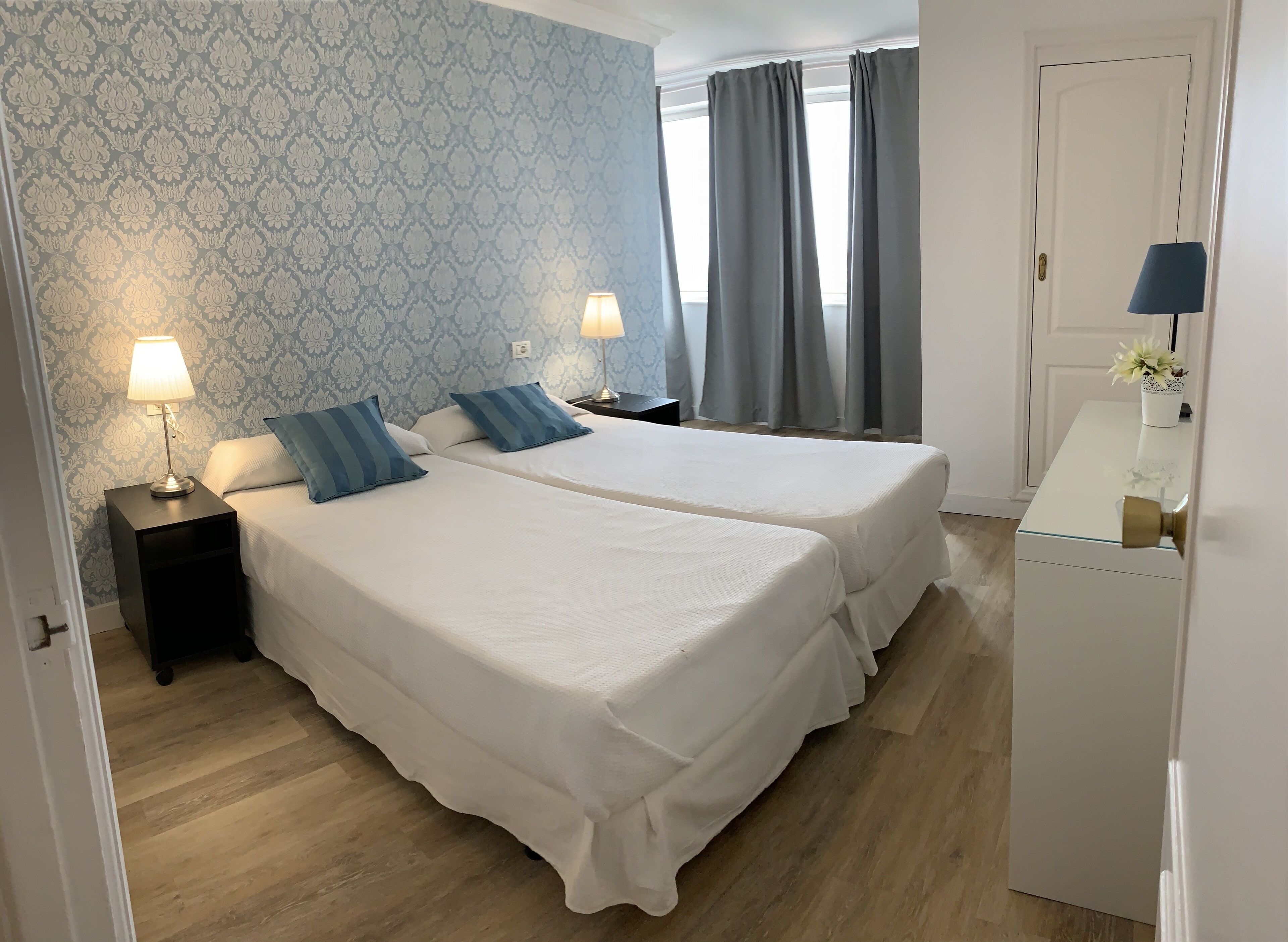 A hotel room with two beds, a nightstand with a lamp, a dresser, and a window with curtains.