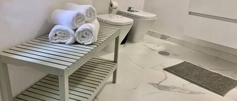 Un baño con suelo de mármol, inodoro, lavabo y toallero con toallas.