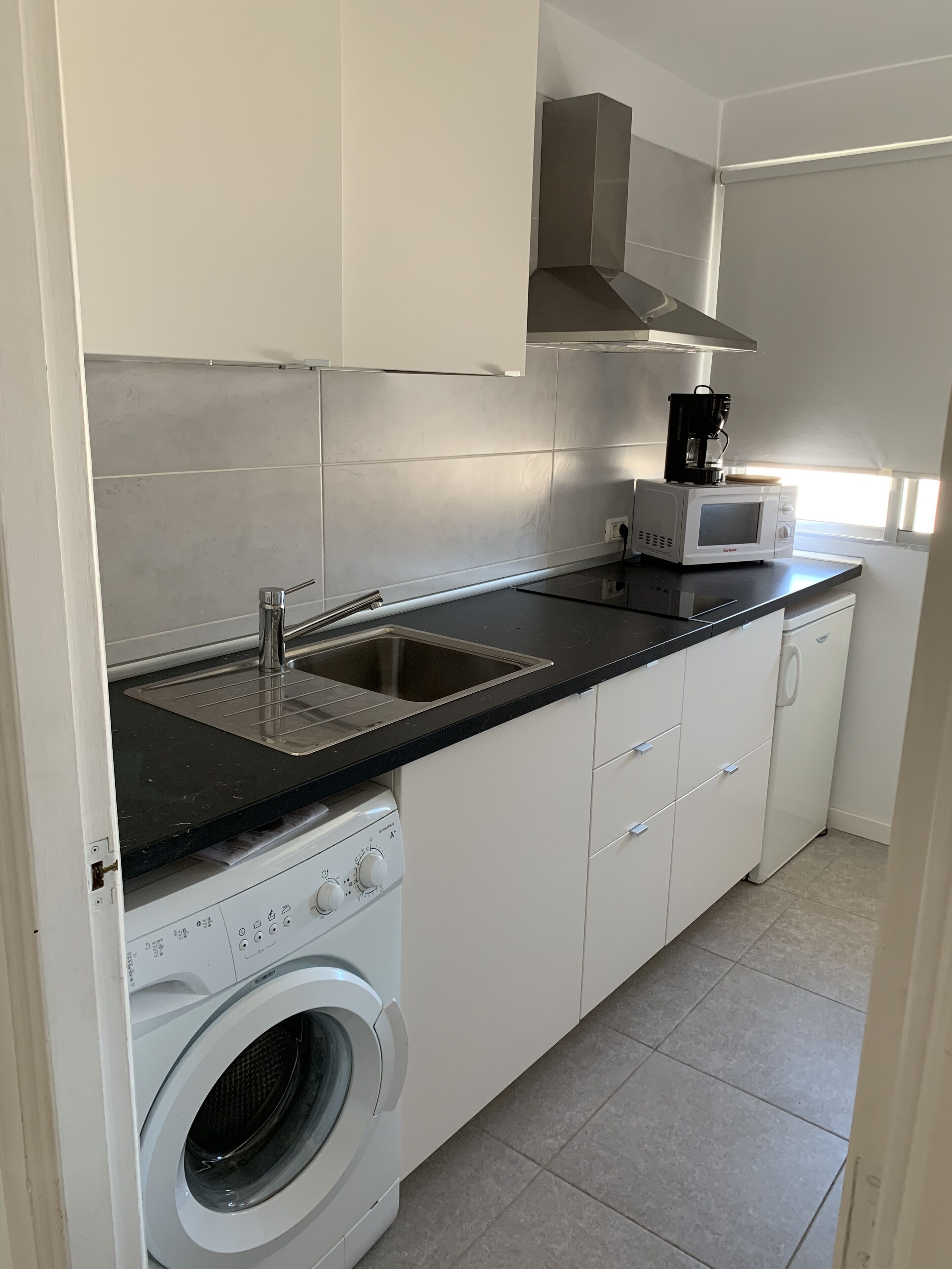 A compact kitchen with a washing machine, a microwave, and a coffee maker.