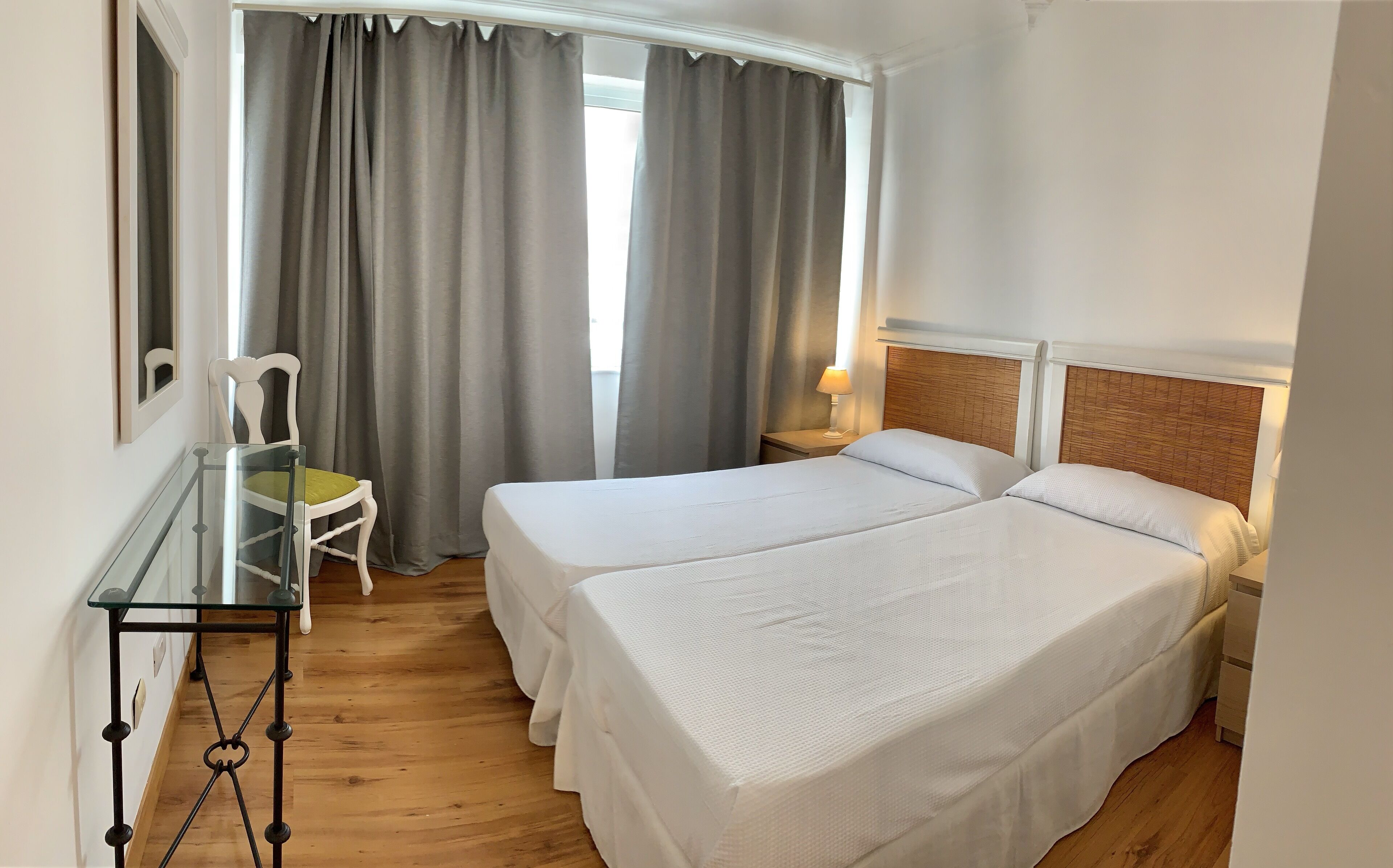 Une chambre d’hôtel avec deux lits, une petite table avec une chaise et une fenêtre avec des rideaux.