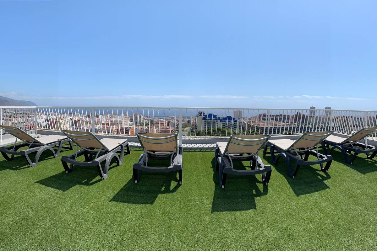Eine Dachterrasse mit Kunstgrasanlage und Liegestühlen mit Blick auf Stadt und Meer.