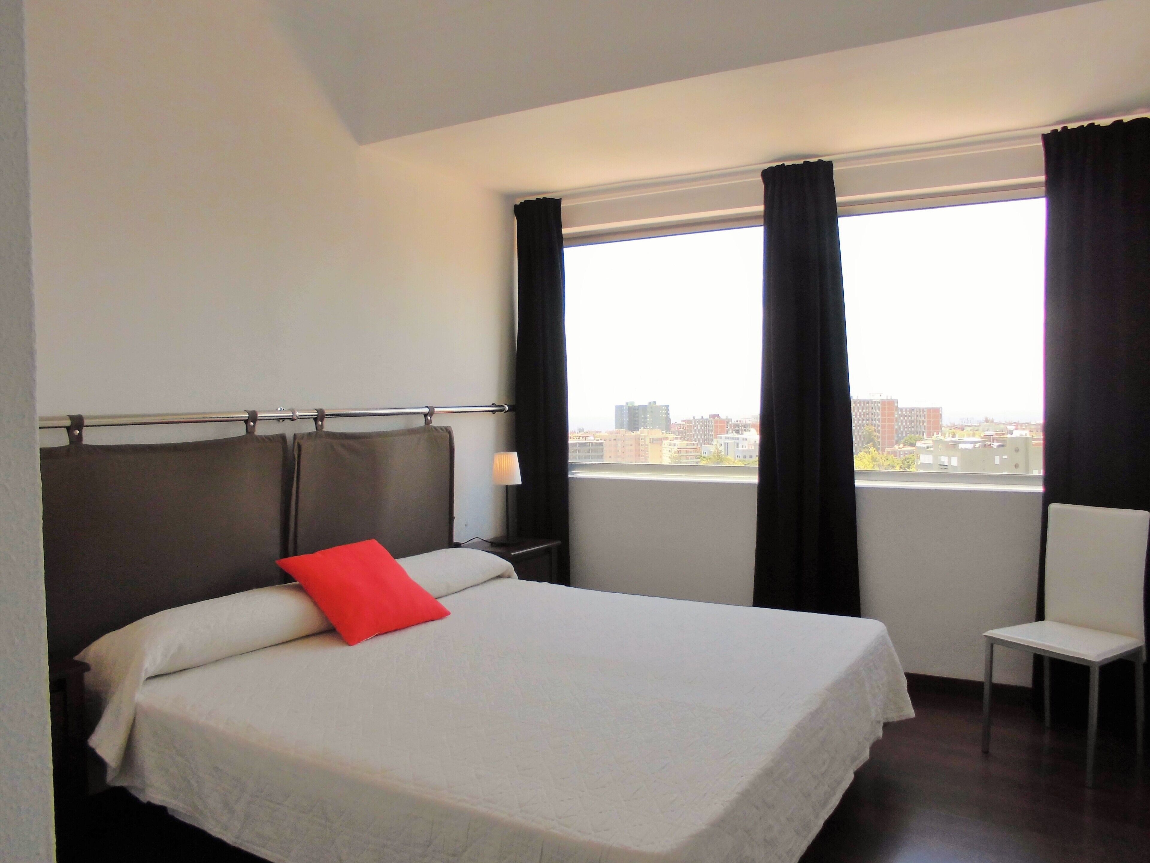 Una habitación de hotel con cama, una silla, una mesita de noche y una ventana con cortinas.