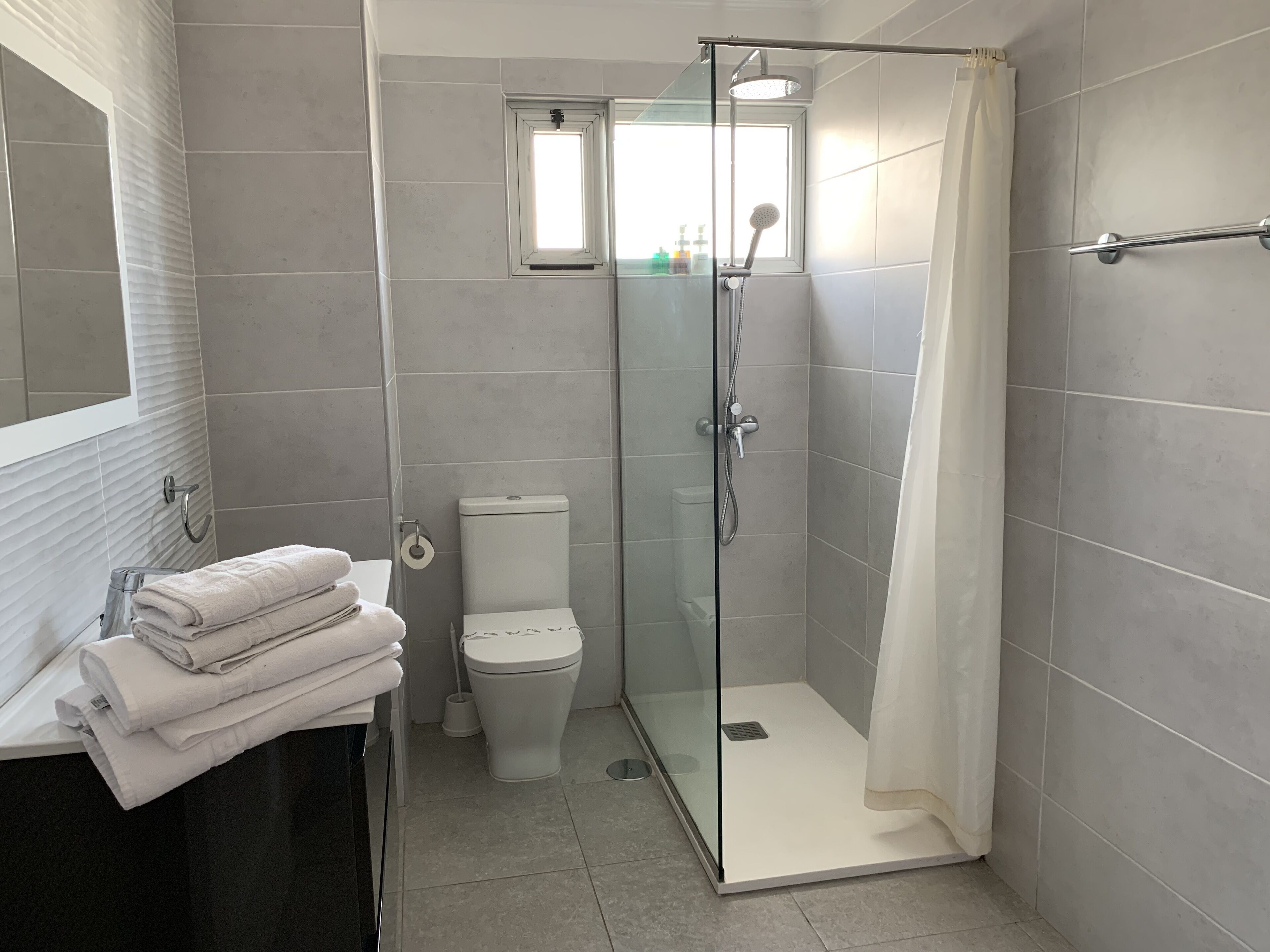 Un bagno moderno con doccia vetro, un water e un lavandino con asciugamani impilati.