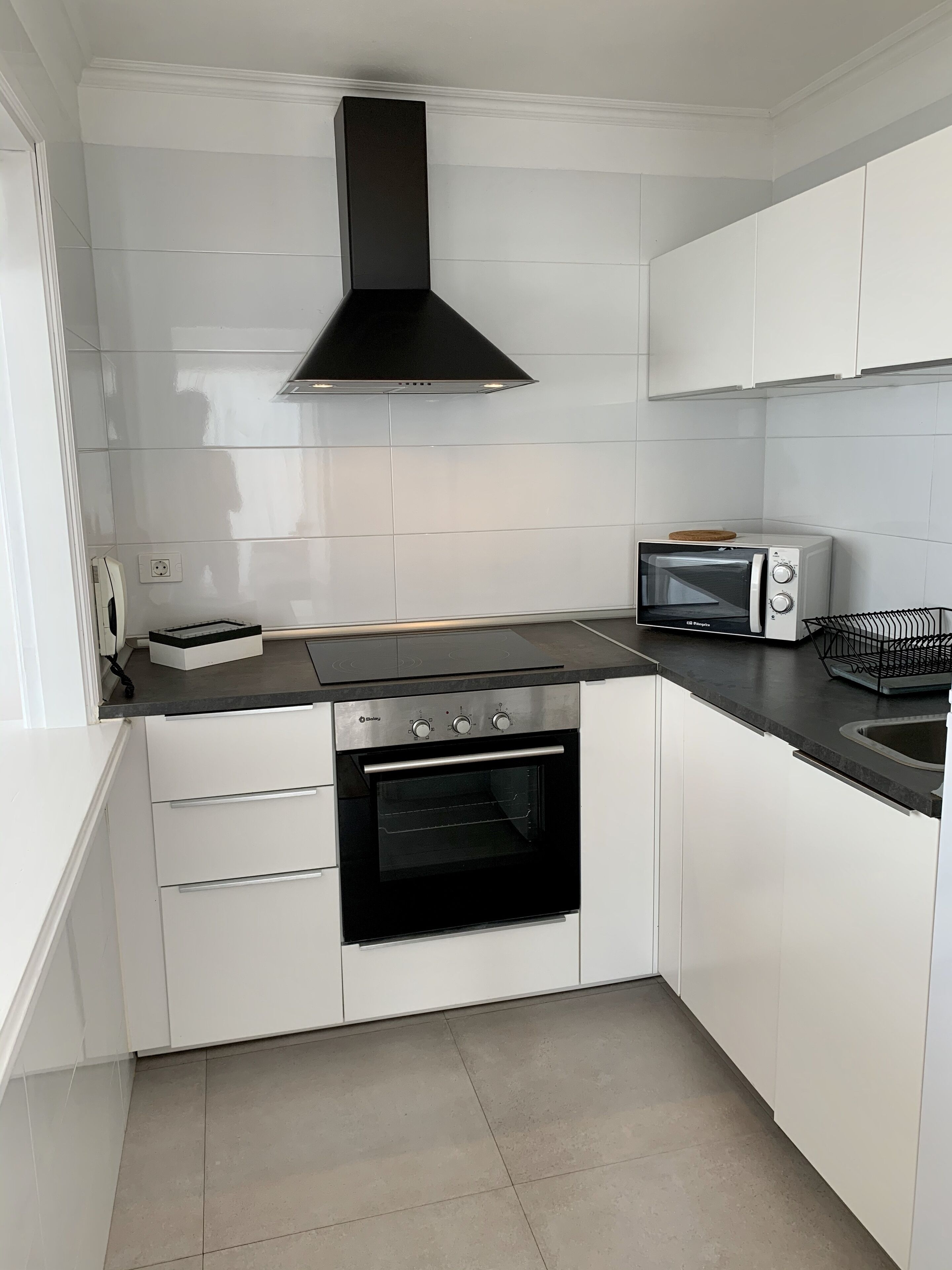 A modern kitchen with white cabinets, a black stove, a microwave, and a black range hood.