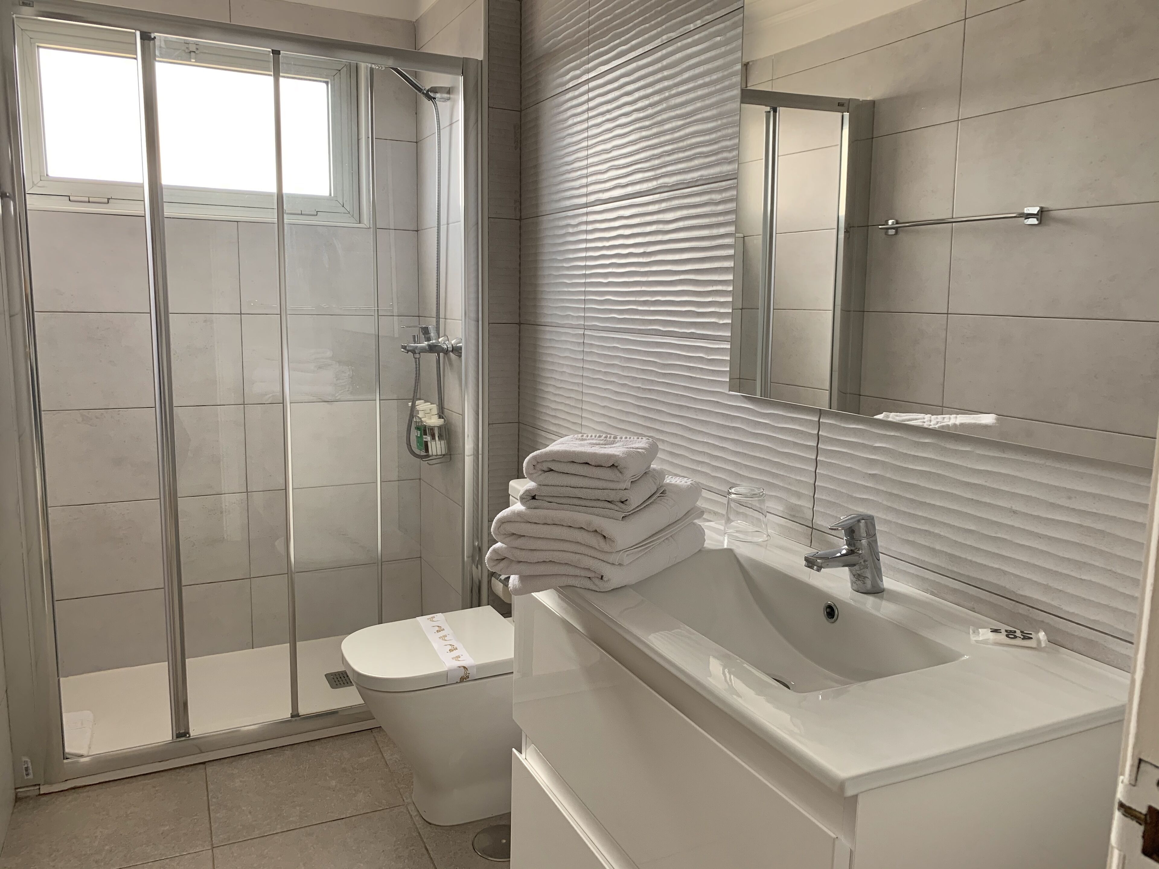 A modern bathroom with a glass-enclosed shower, a white sink, and a toilet with a towel on top.