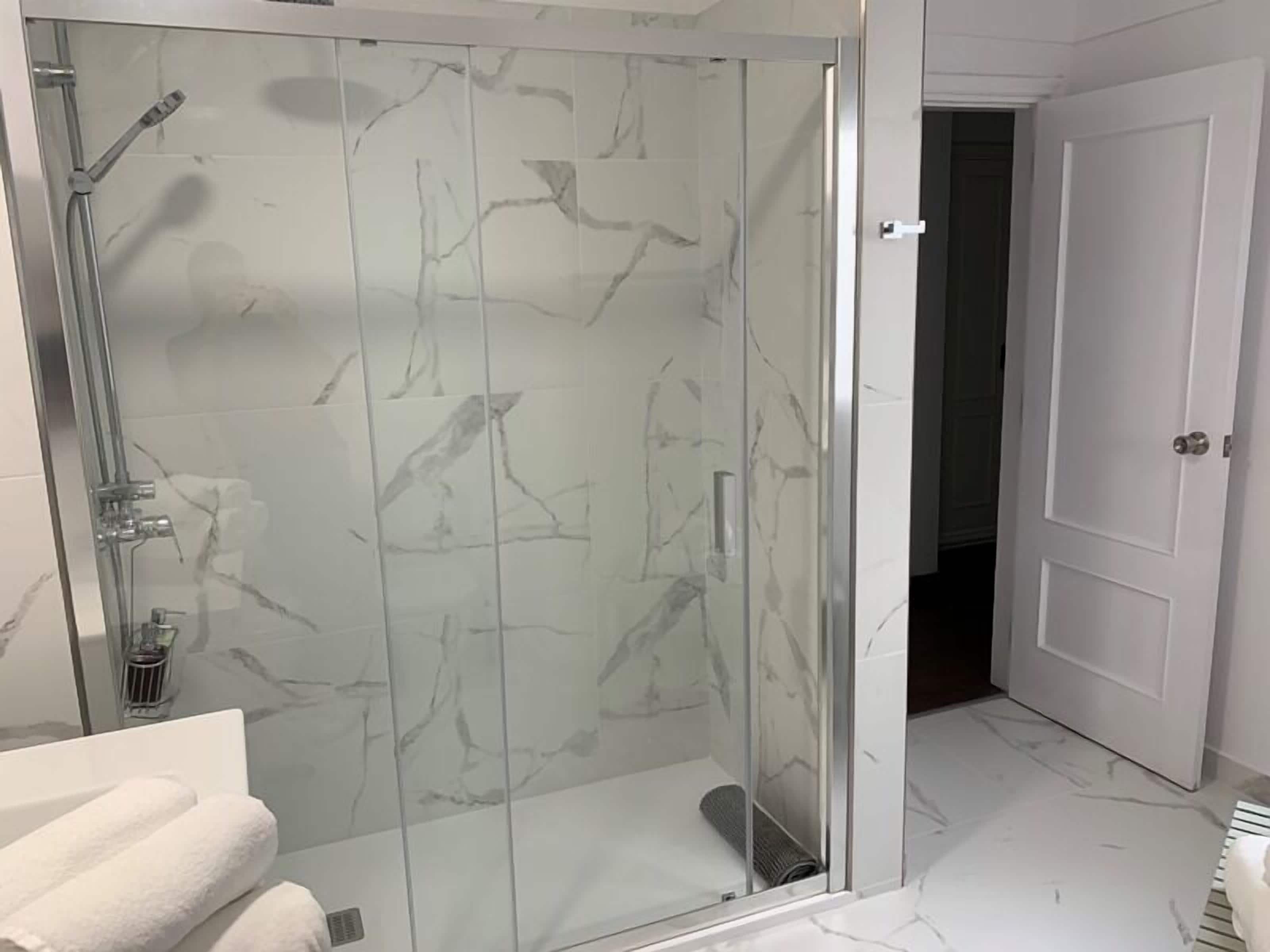 Un baño moderno con cabina de ducha de vidrio, baldosas de mármol y una puerta blanca.