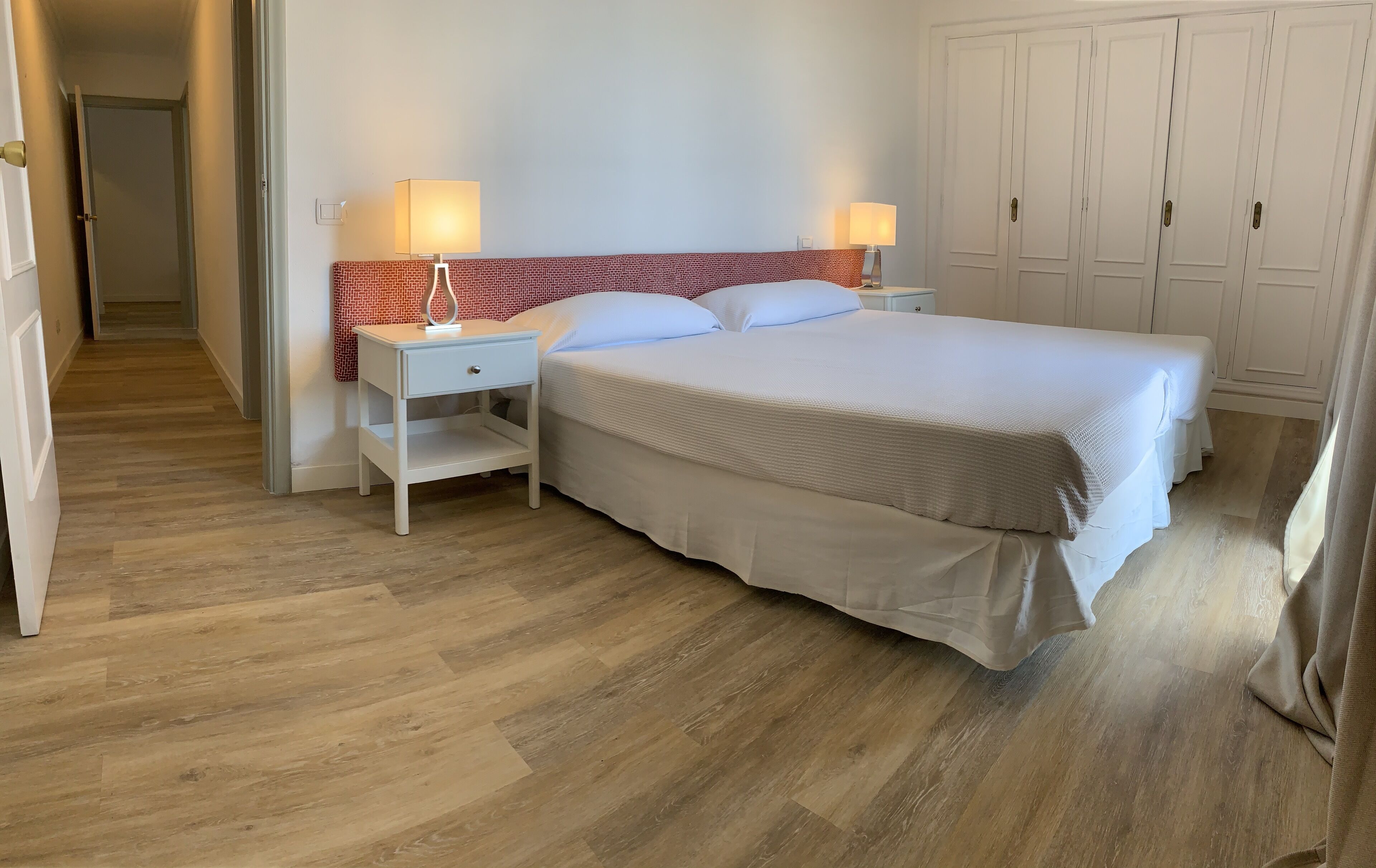A neatly arranged hotel room with a large bed, two bedside tables with lamps, a red patterned headboard, and a wardrobe.