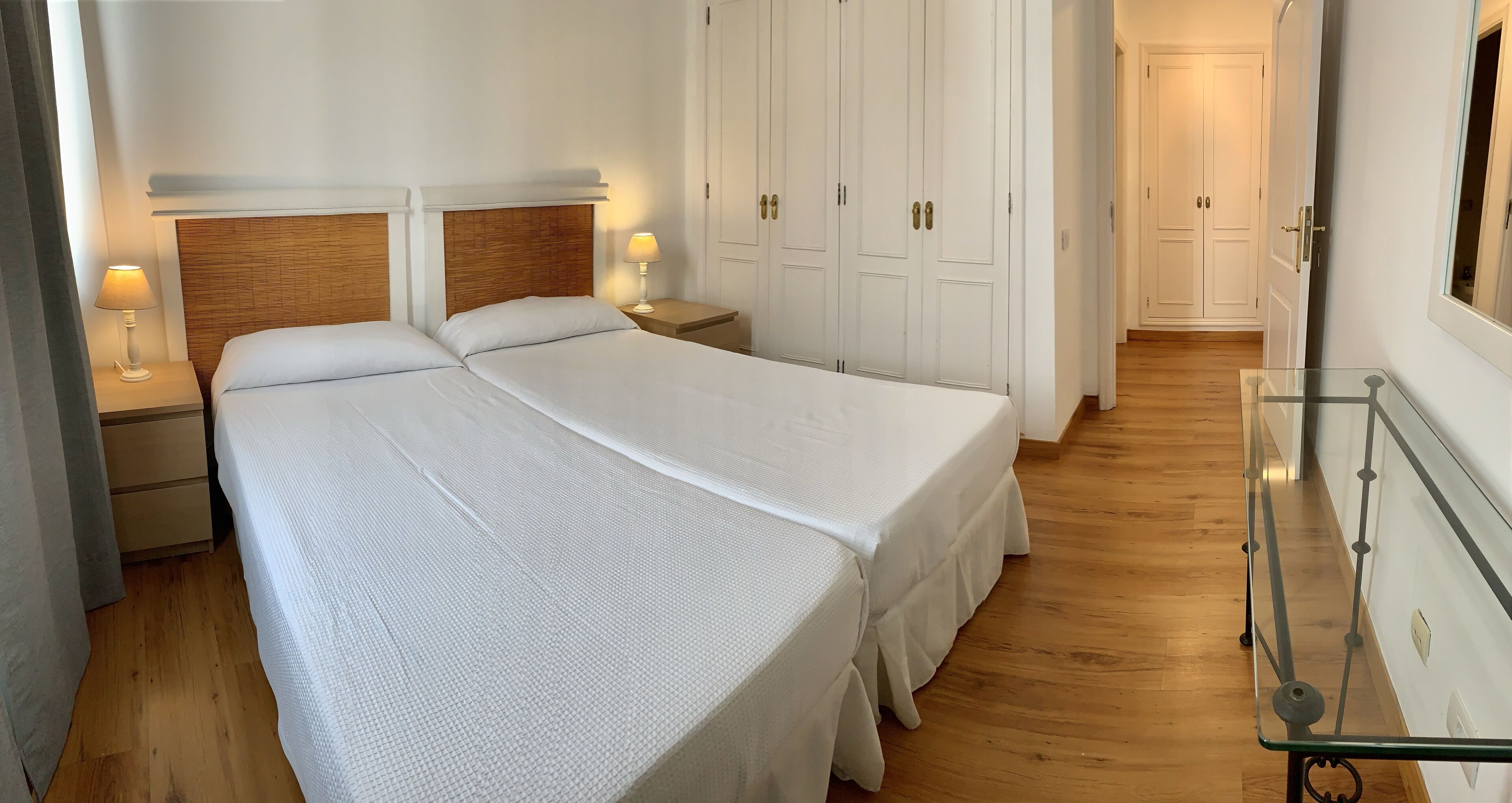 A bedroom with two beds, wooden flooring, white walls, and a glass table.