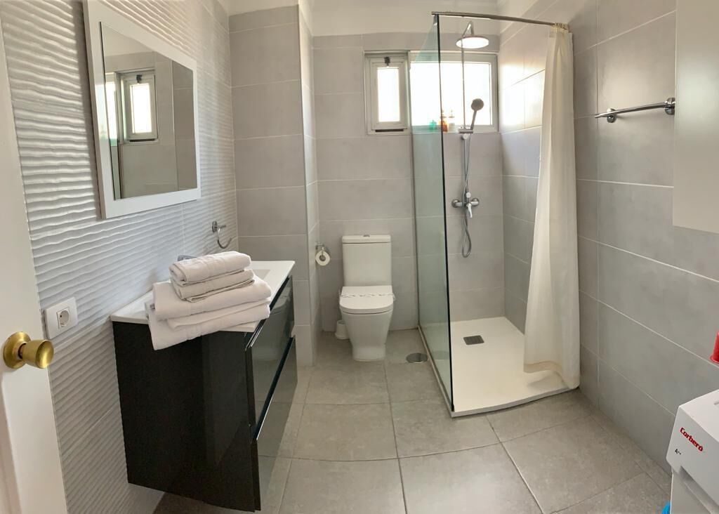 Un baño moderno con ducha de vidrio, inodoro y tocador con espejo y una pila de toallas.