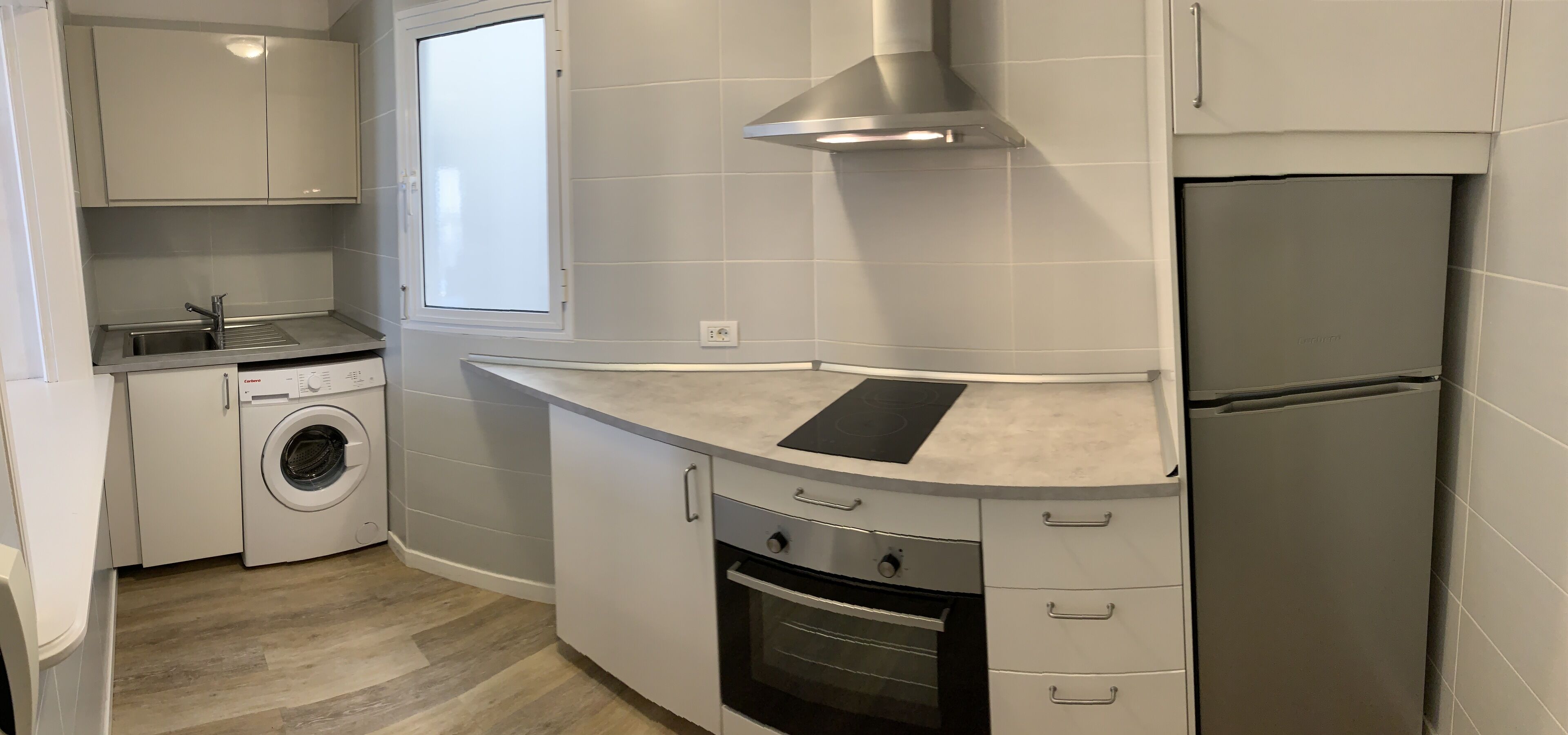 A compact kitchen with a built-in washing machine, a stainless steel refrigerator, and a modern stove.