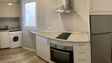 A compact kitchen with a built-in washing machine, a stainless steel refrigerator, and a modern stove.