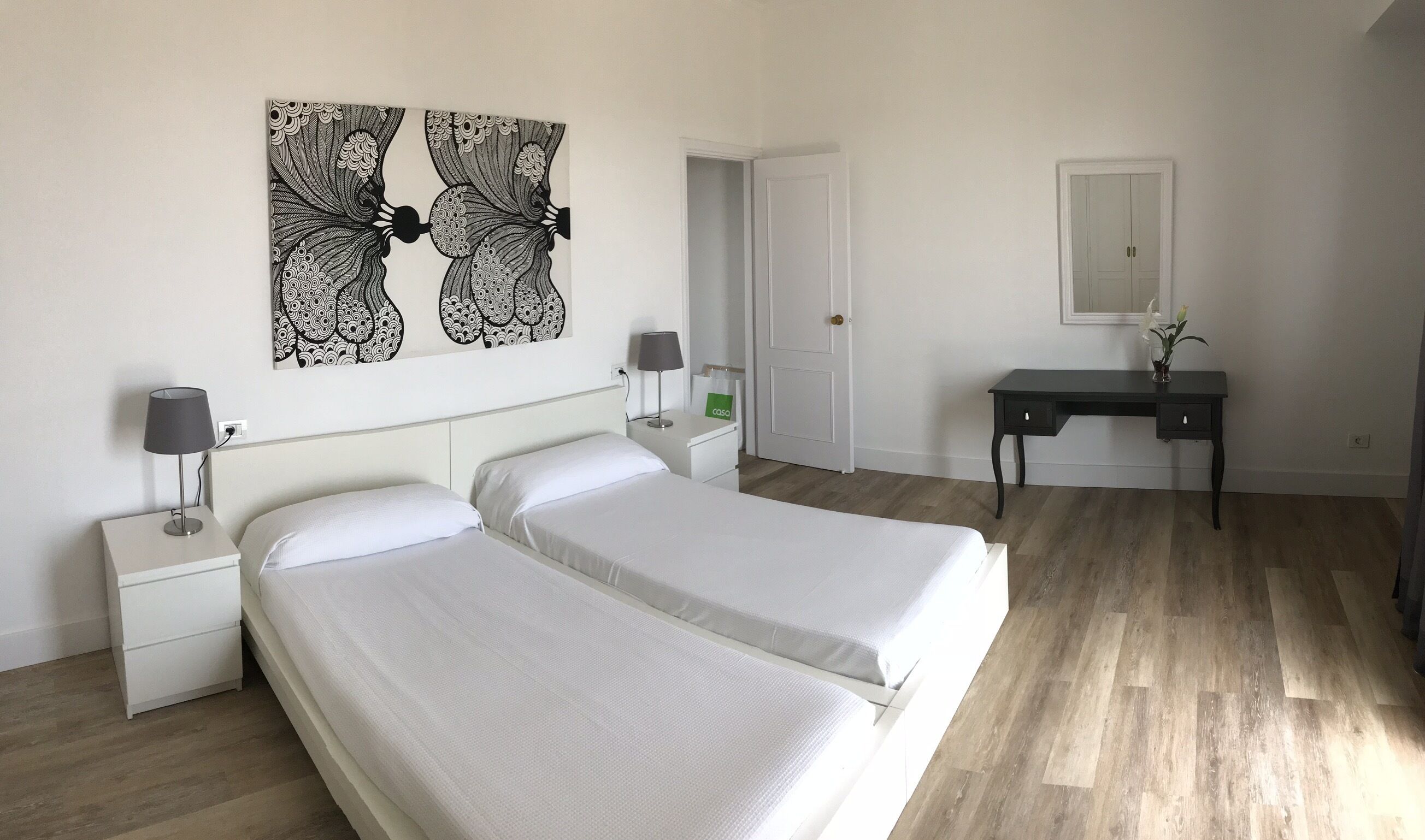 A hotel room with two beds, a desk, a chair, a lamp, and a wall art piece.
