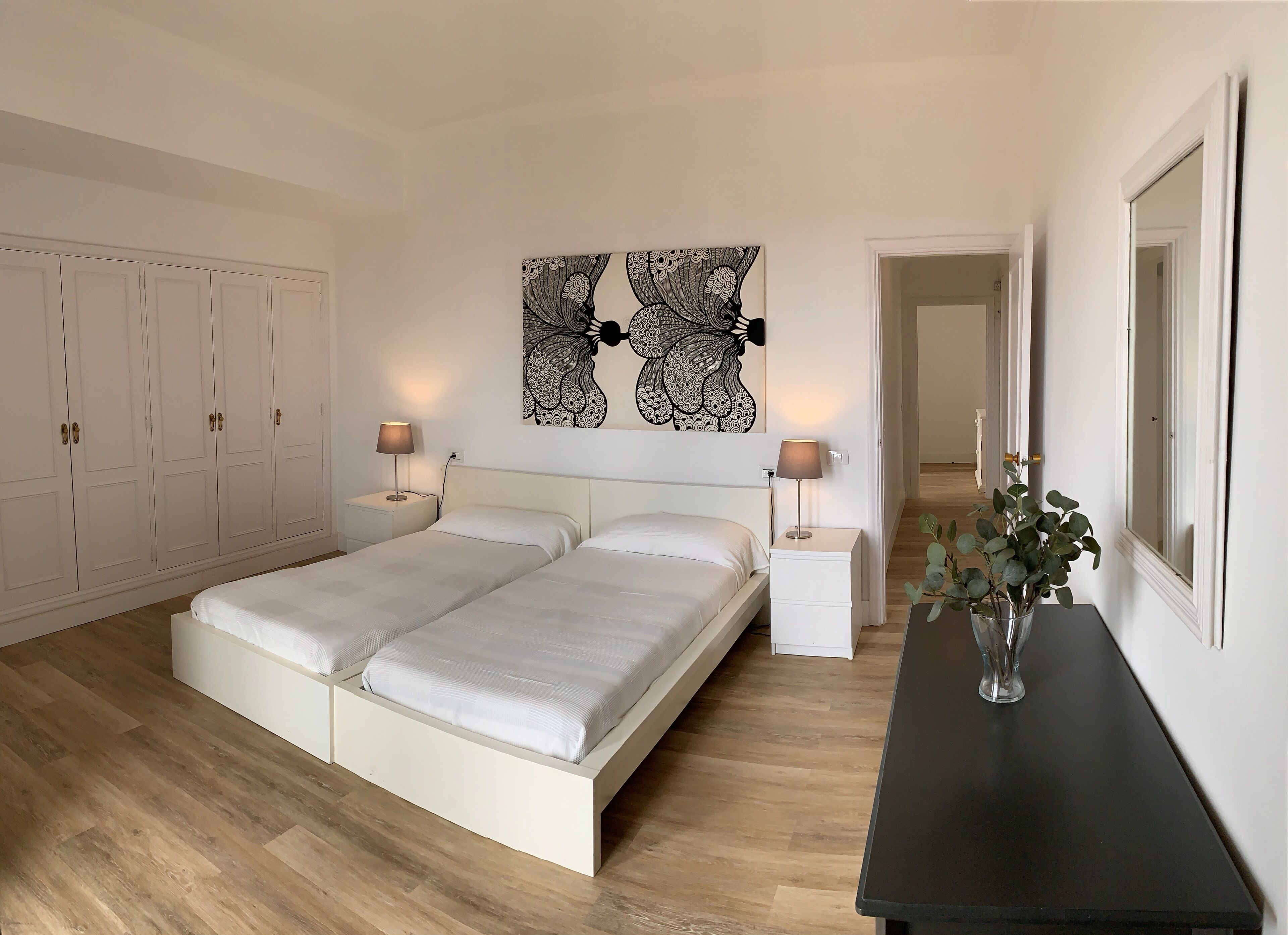 Une chambre à coucher avec un lit double, deux tables de chevet avec des lampes, une grande œuvre d’art abstraite accrochée au mur et une armoire.