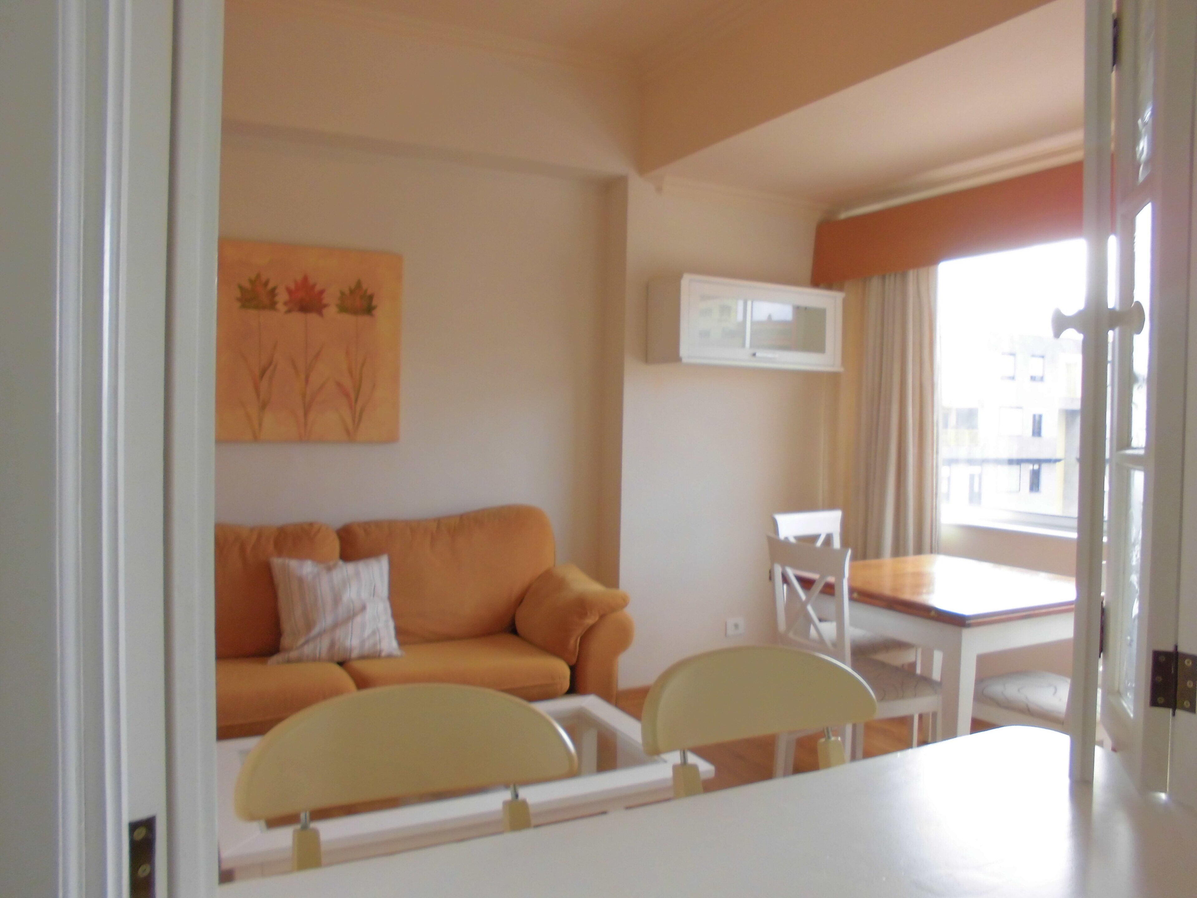 Una habitación con sofá, una mesa de comedor con sillas, microondas y ventana con cortinas.