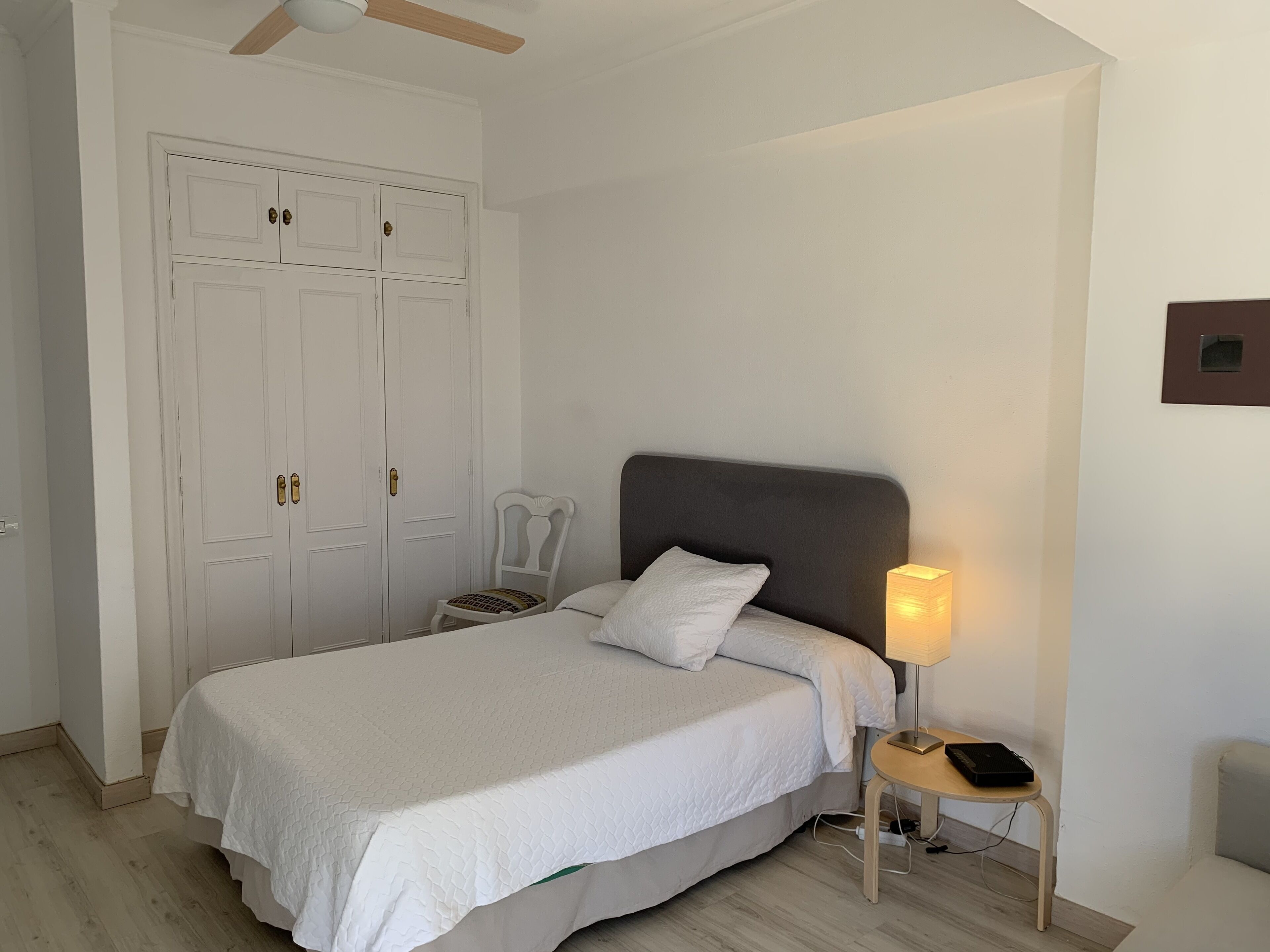 A bedroom with a bed, a nightstand with a lamp, and a wardrobe.