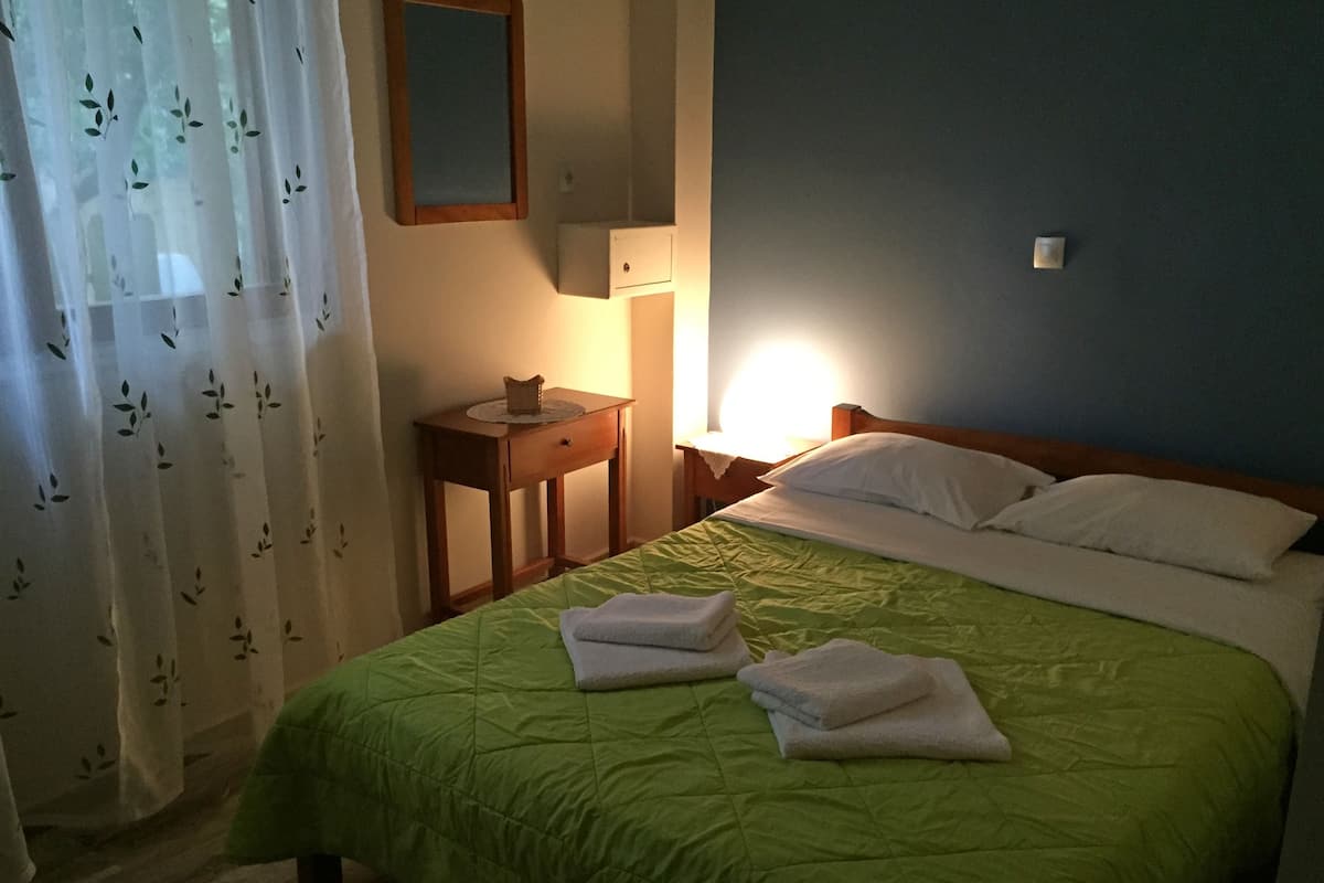 Una cama bien hecha con ropa de cama verde y almohadas blancas, una mesita de noche con lámpara y un espejo en la pared.