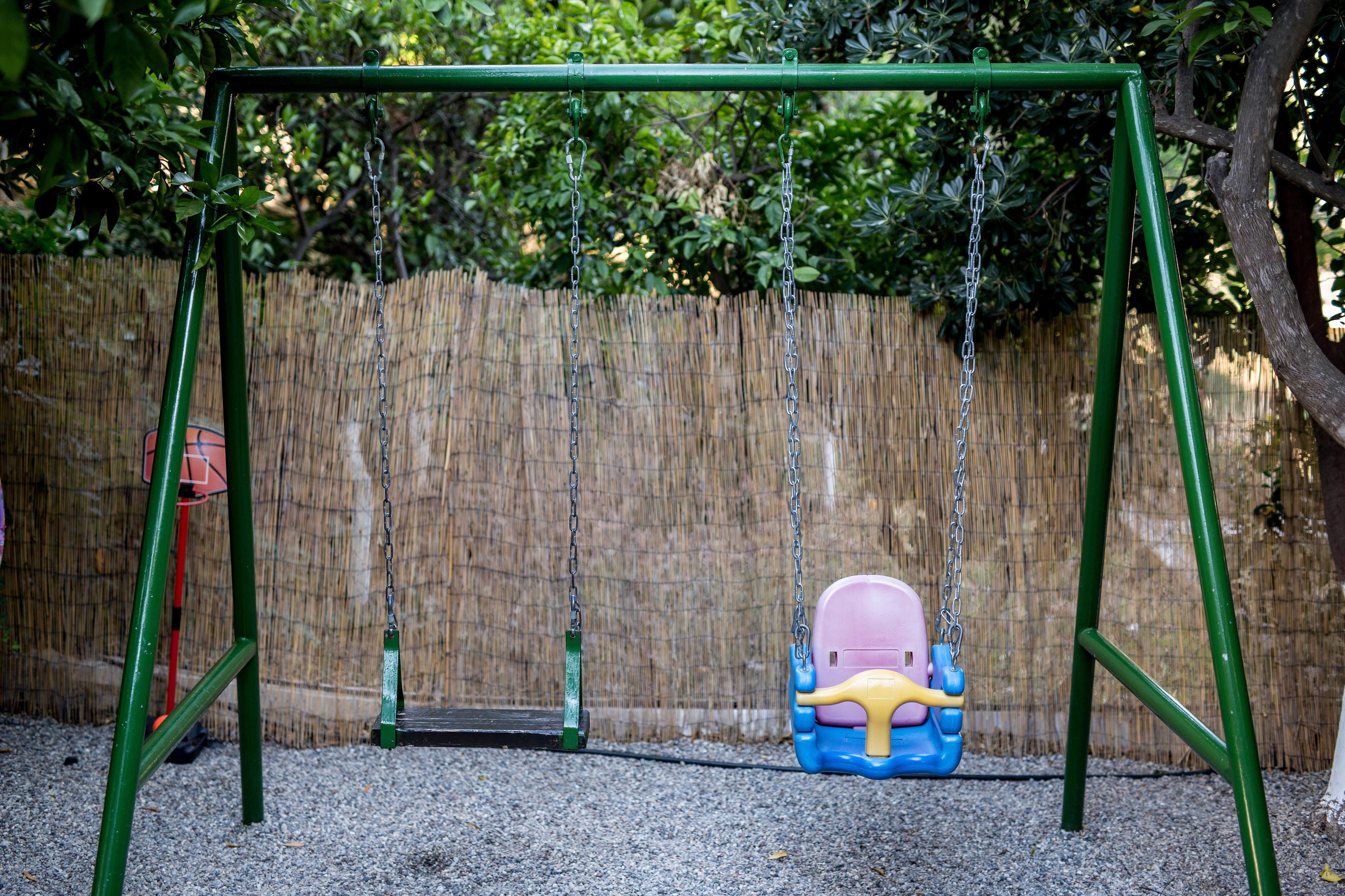 Un columpio con estructura verde y asiento en tonos azul y rosa.
