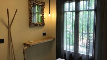 Hotellihuone, jossa on sänky, yöpöytä, peili ja ikkuna, jossa on läpikuultavat verhot.