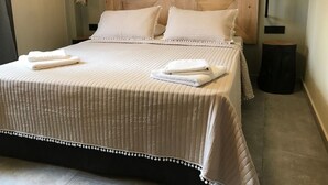 Una cama bien hecha con tablero de madera, dos almohadas y dos toallas dobladas.