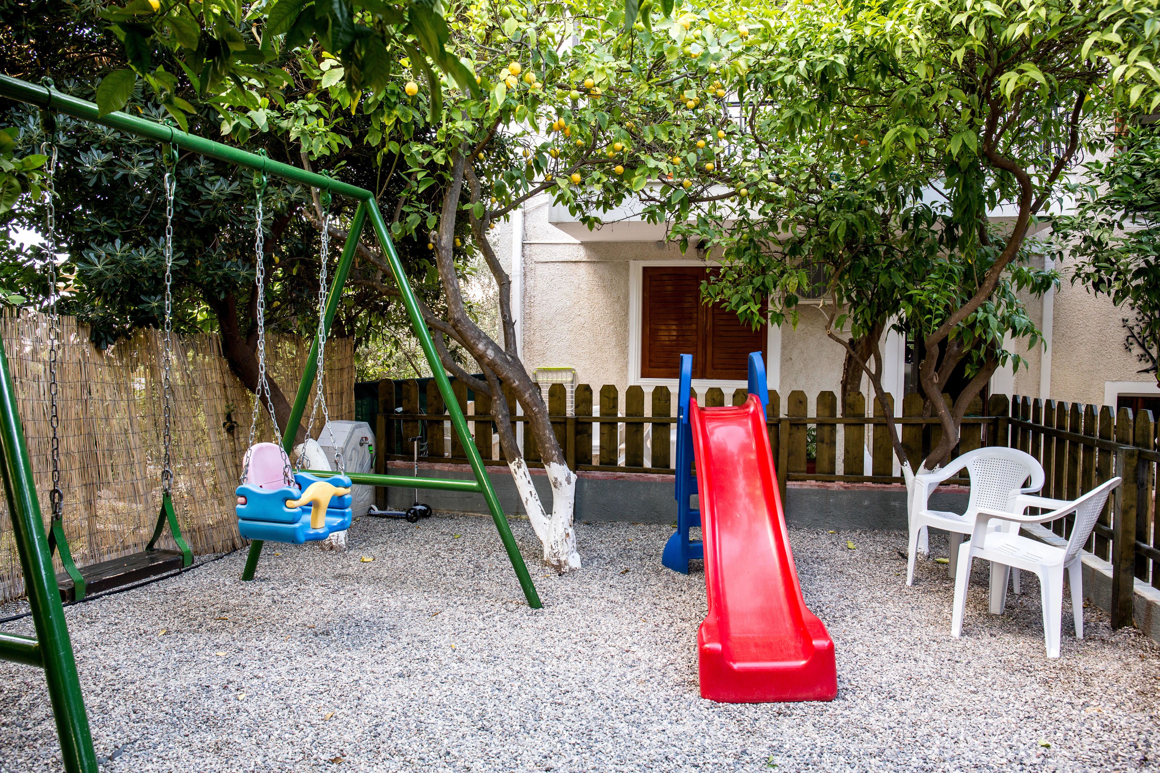 A playground with swings, a slide, and a fence.