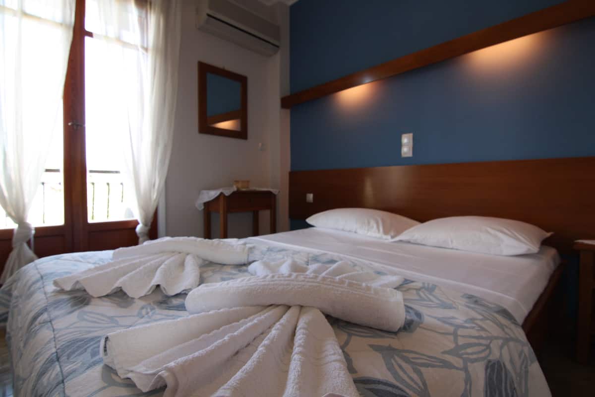Una habitación de hotel con cama, mesita de noche, espejo y ventana con cortinas.