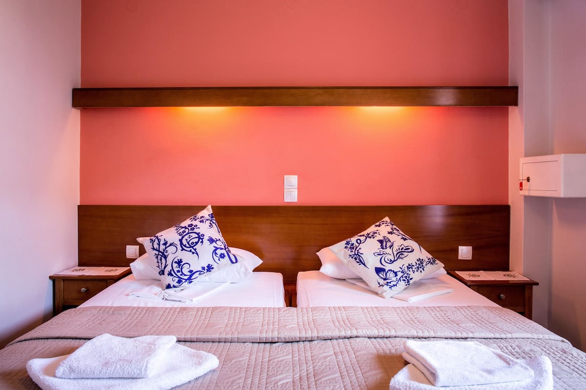 Habitación de hotel con dos camas, cada una con cabecero de madera, ropa de cama blanca y almohadas estampadas en azul. Hay dos mesitas de noche con lámparas, y una colcha grande con diseño acolchado.
