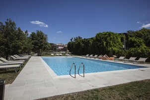 A rectangular swimming pool with clear blue water, surrounded by a paved deck with lounge chairs.