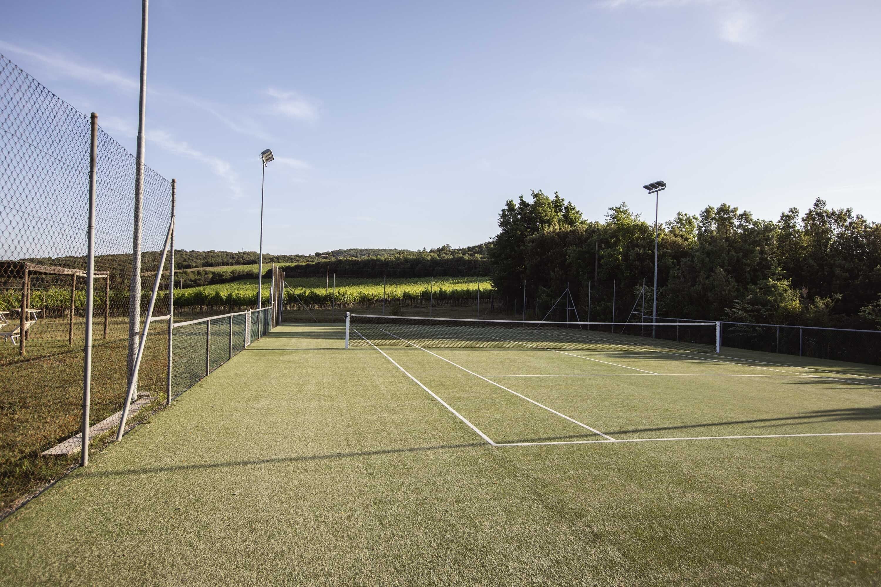 A tennis court with a chain-link fence, floodlights, and a net.