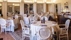 Un área de comedor con mesas y sillas blancas, un espejo grande y una botella de vino sobre una mesa.